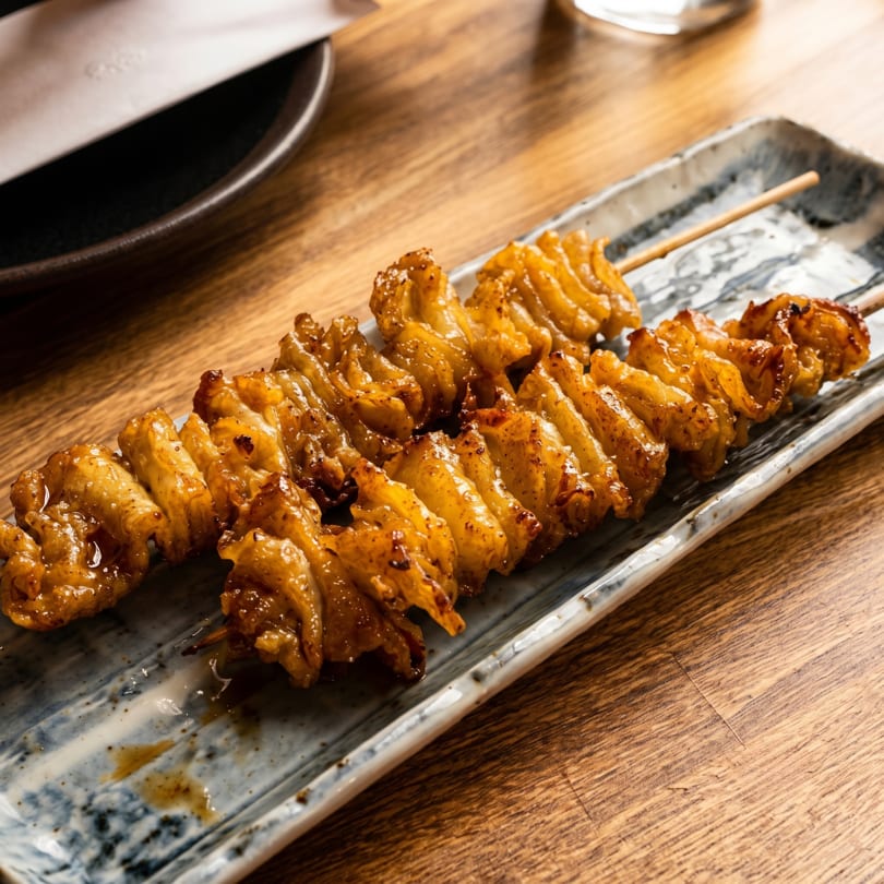 Two skewers of grilled, golden-brown chicken skin yakitori on a rectangular ceramic plate.