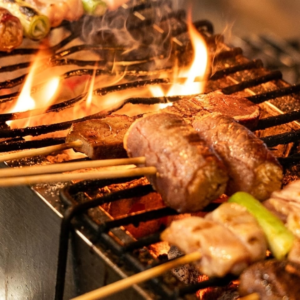 Skewers of meat and vegetables grilling over open flames on a yakitori grill.