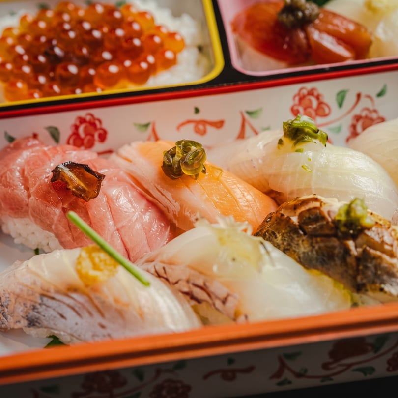Close-up of a bento box filled with various types of sushi, including salmon, tuna, and white fish.