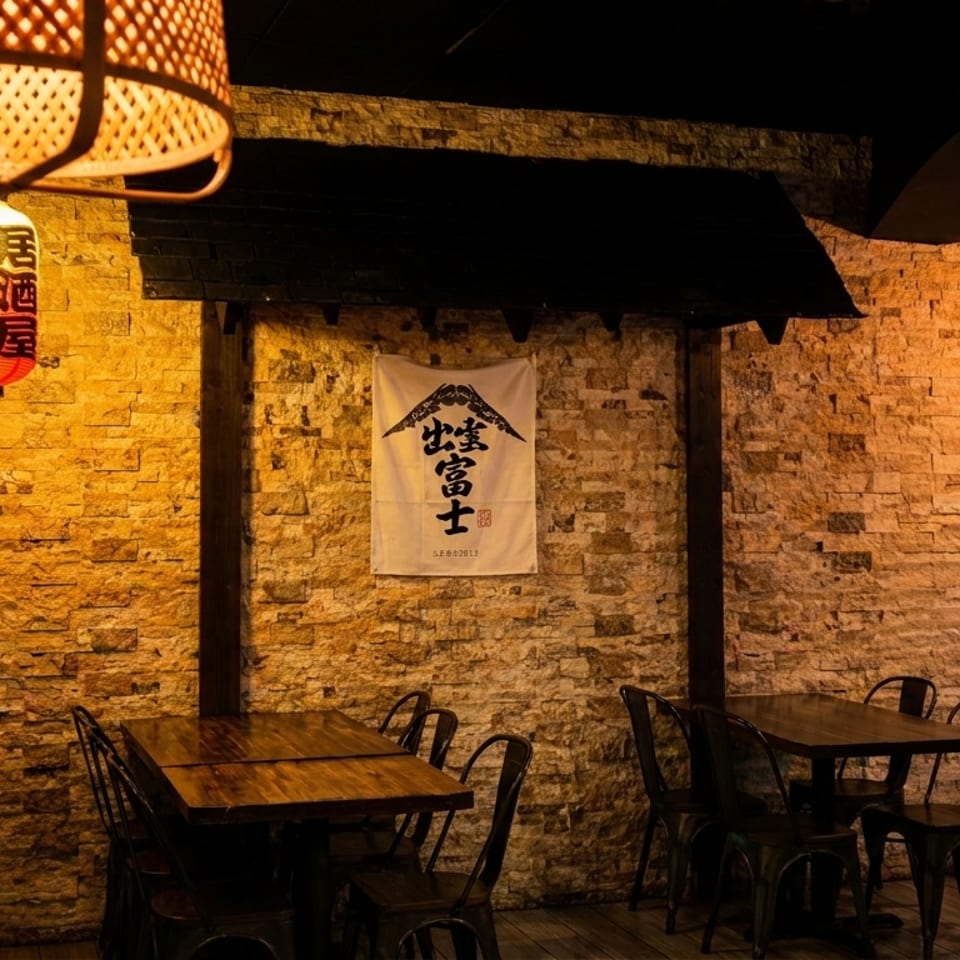 Warmly lit Japanese restaurant interior with stone walls, wooden tables, metal chairs, and hanging lanterns.