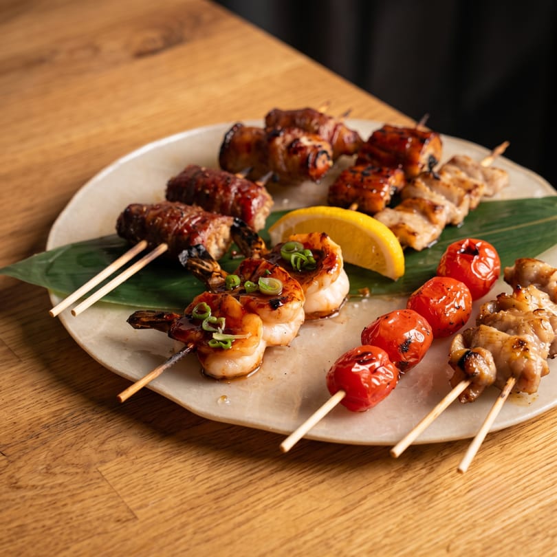 A plate of grilled skewers with shrimp, bacon-wrapped meat, chicken, and cherry tomatoes.
